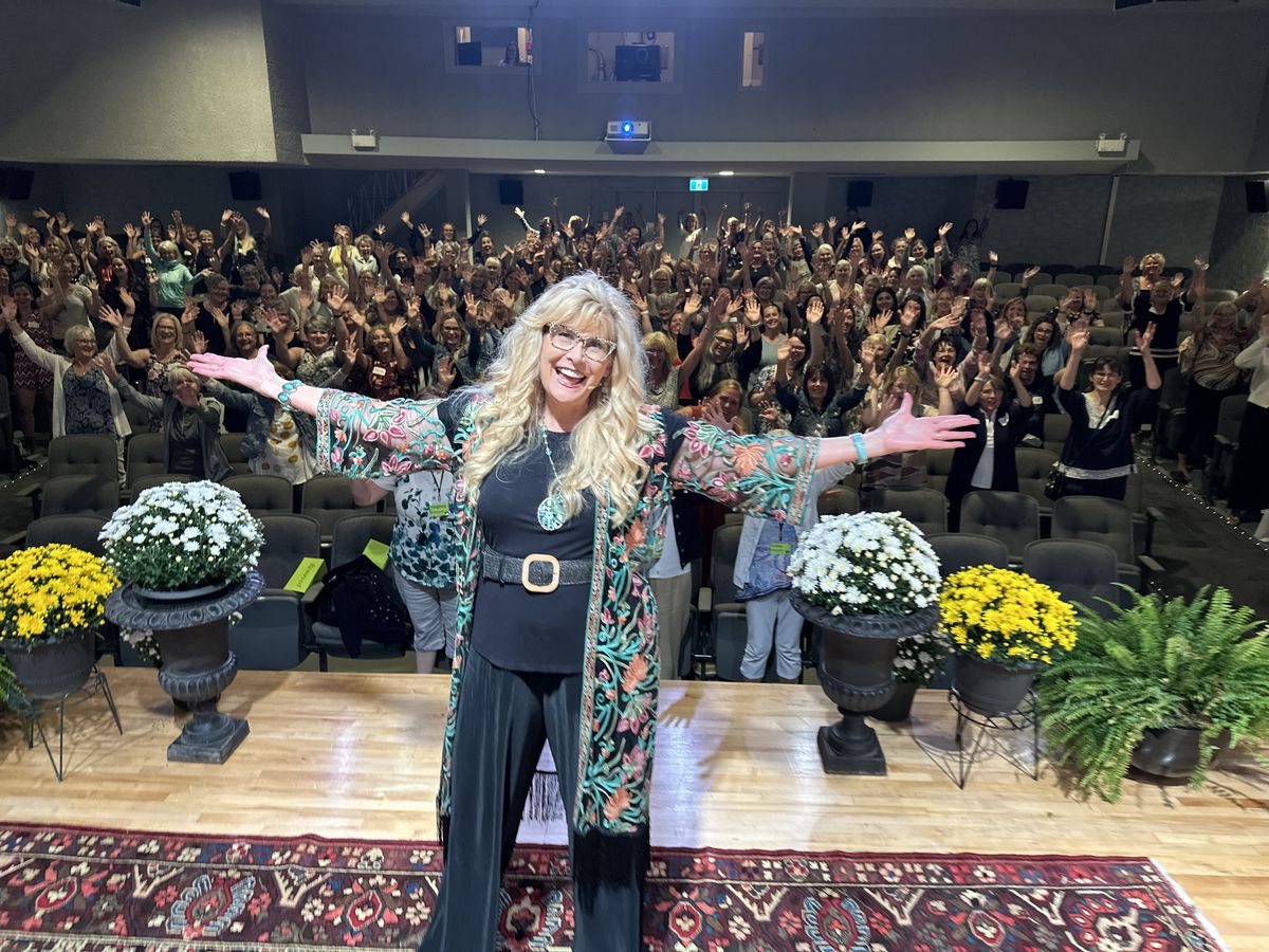 Robyn speaking to a full auditorium of women with their hands raised